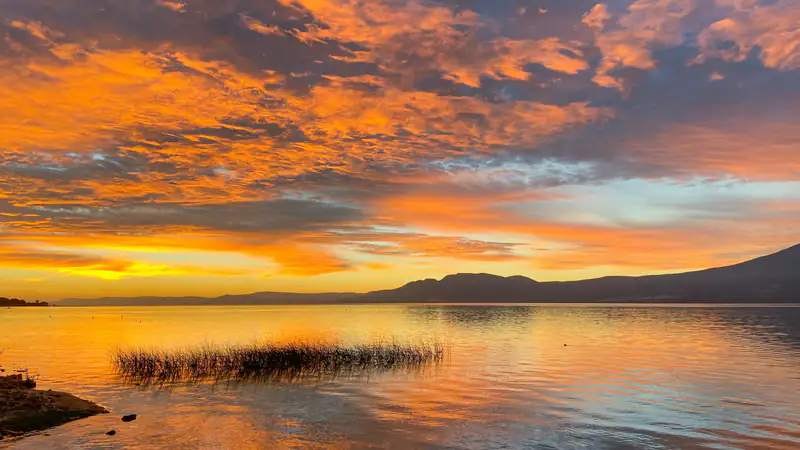 Amanecer sobre el Lago de Chapala con el cielo naranja reflejado en el agua