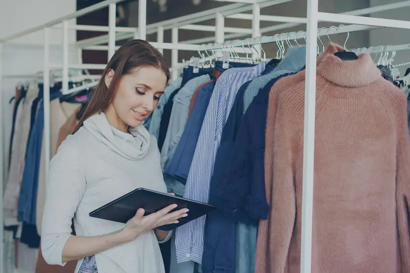 Emprendedora revisando su catálogo en una tableta dentro de su tienda de ropa